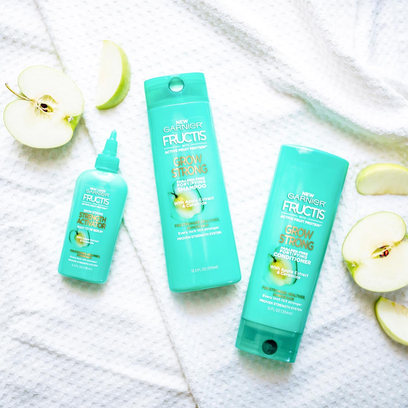 Garnier Fructis Grow Strong Shampoo, Fructis Grow Strong Conditioner, and Fructis Strength Activator on white towels beside sliced granny smith apples.